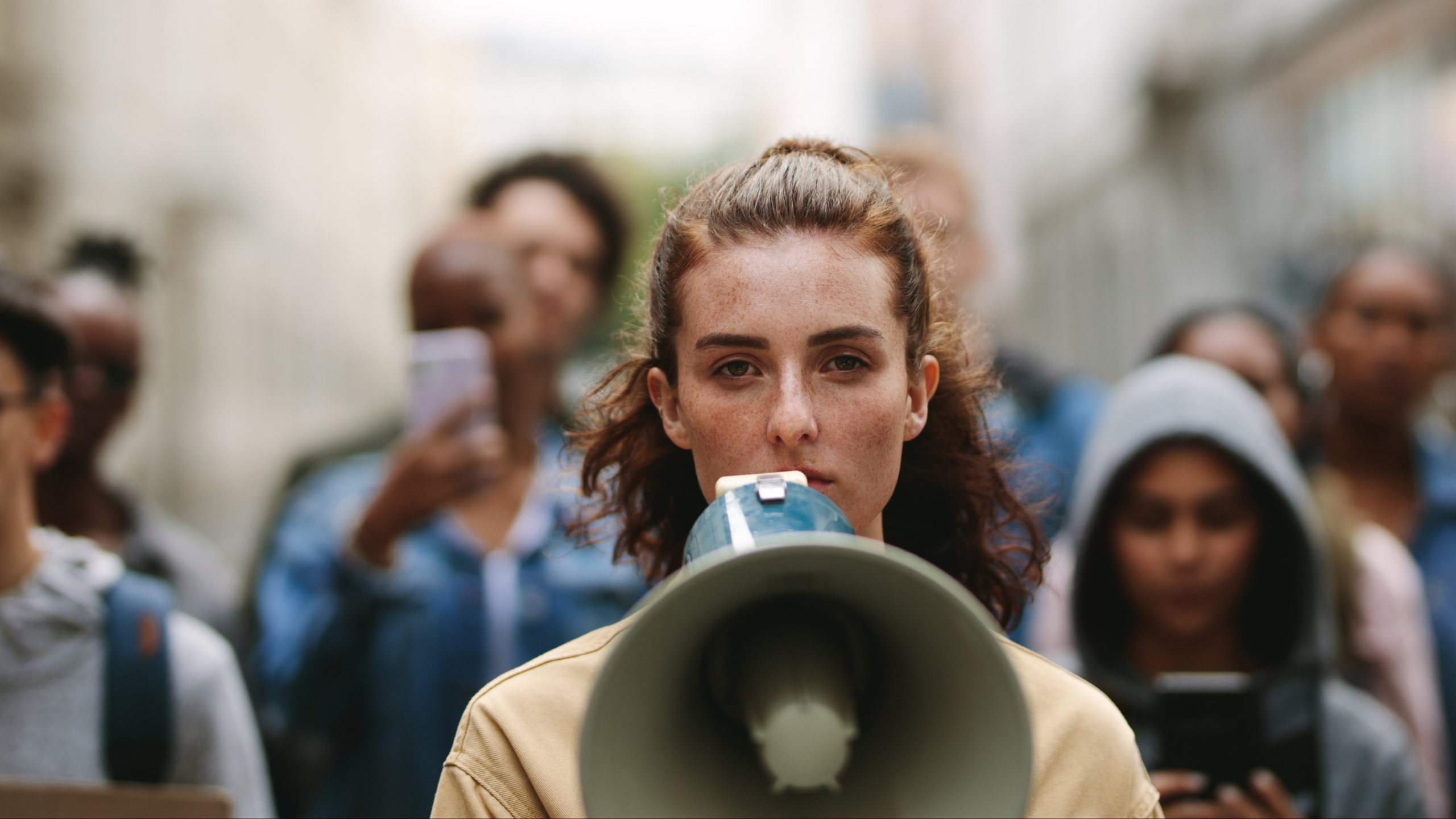 Eine Frau hat ein Megafon vor dem Gesicht. Hinter ihr sind Menschen zu sehen, die in ihre Richtung mitlaufen